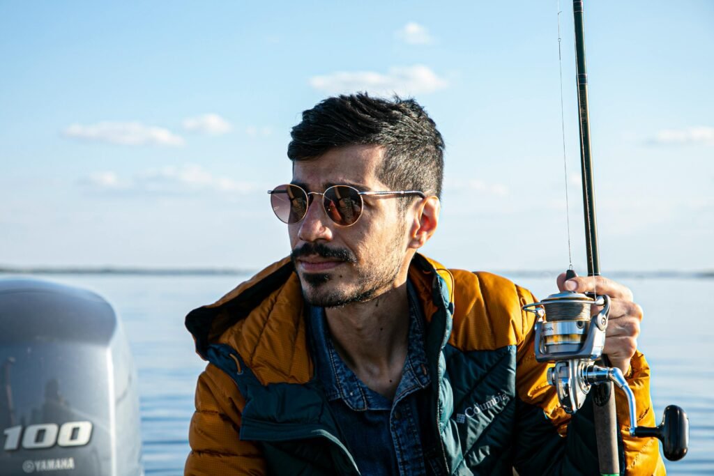 A man wearing sunglasses enjoys fishing on a calm sea during a sunny day.