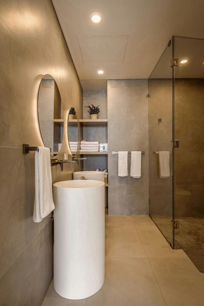 Elegant minimalist bathroom featuring a round lit mirror and sleek fixtures in neutral tones.